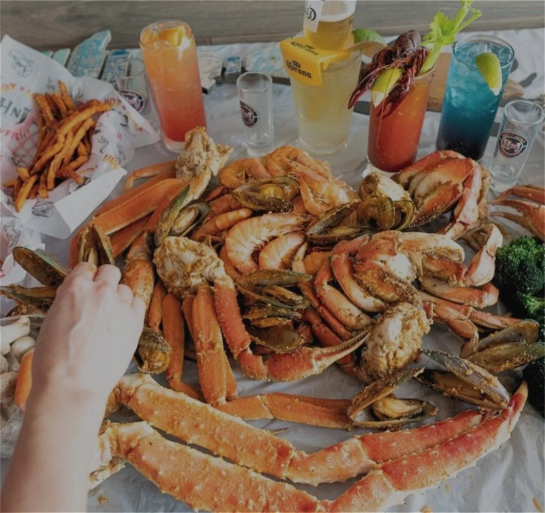 Seafood boil featuring crab legs, shellfish, cocktails, and beer served on a restaurant table.