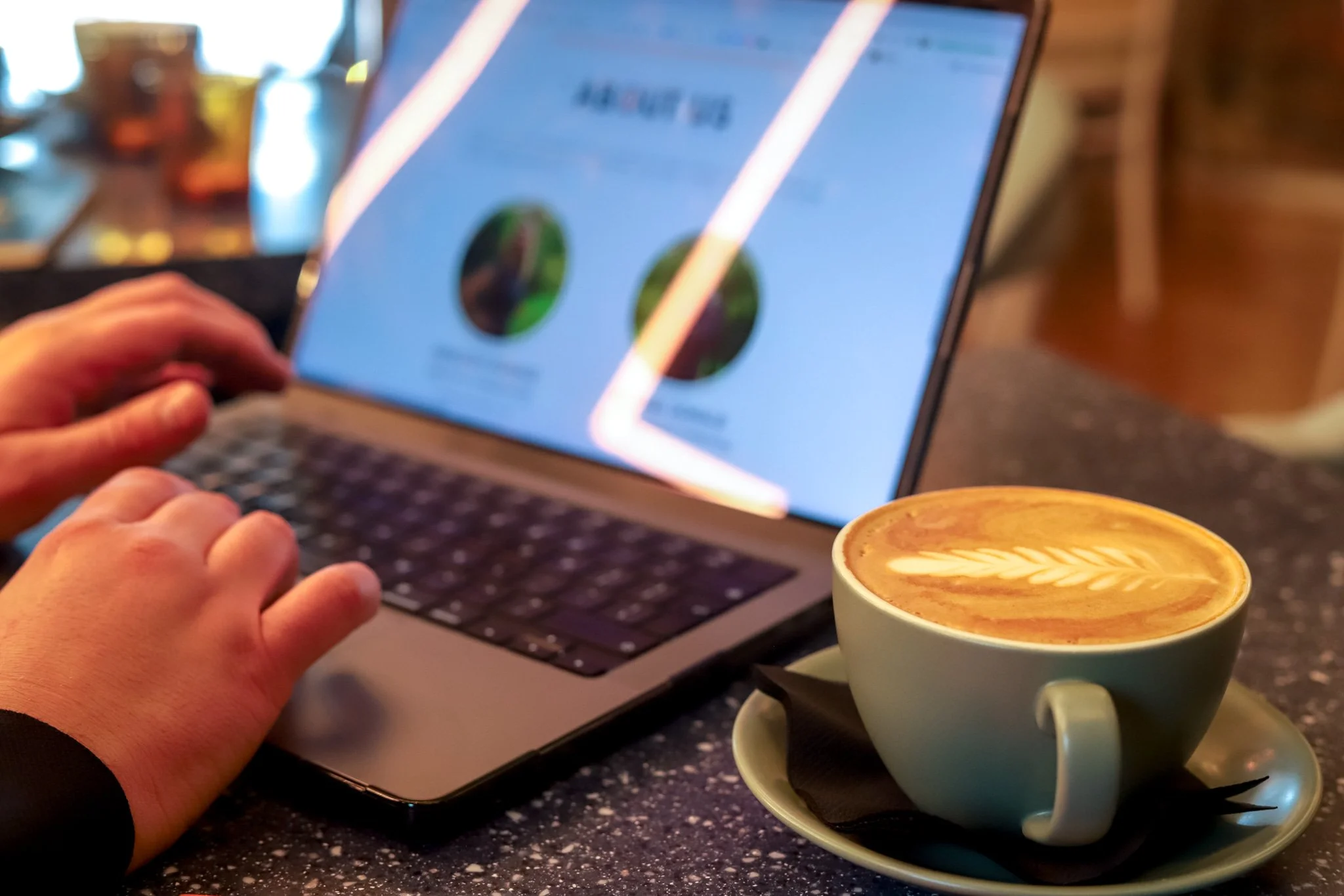 A person using a laptop with a screen showing a website or app, with a cup of coffee with latte art in the foreground.
