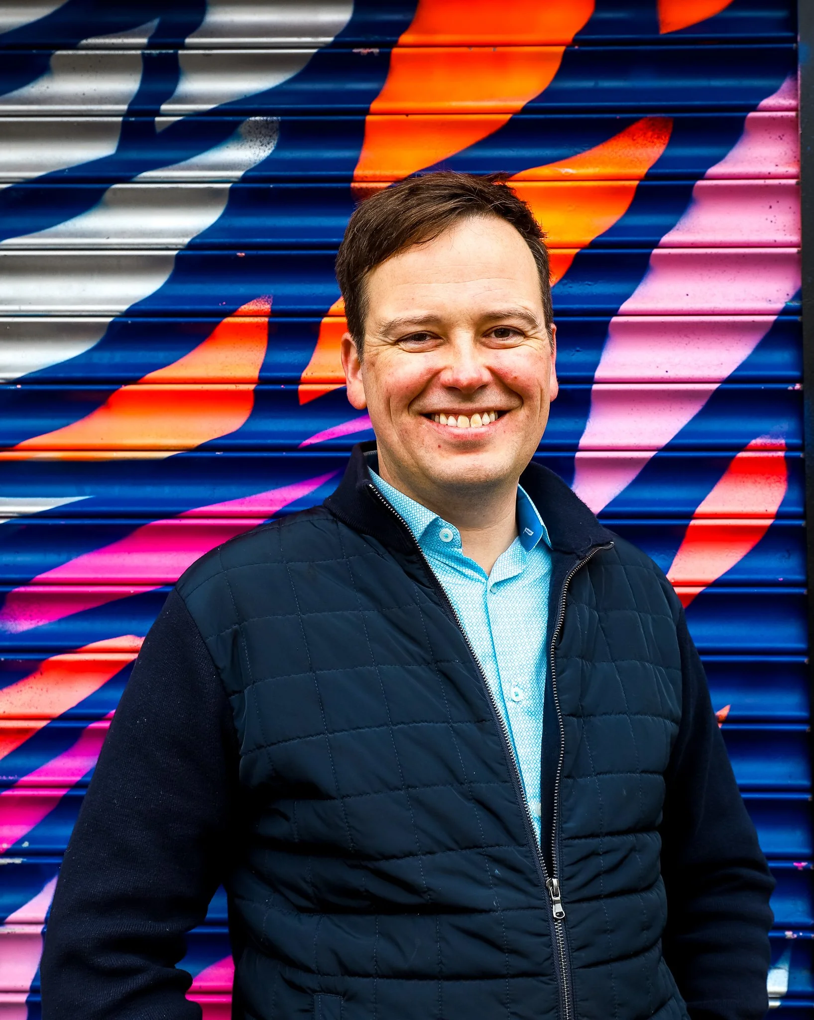 Michael standing in front of a colourful graffiti-covered metal shutter mural.