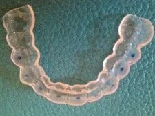 Clear Invisalign retainer on a teal surface.