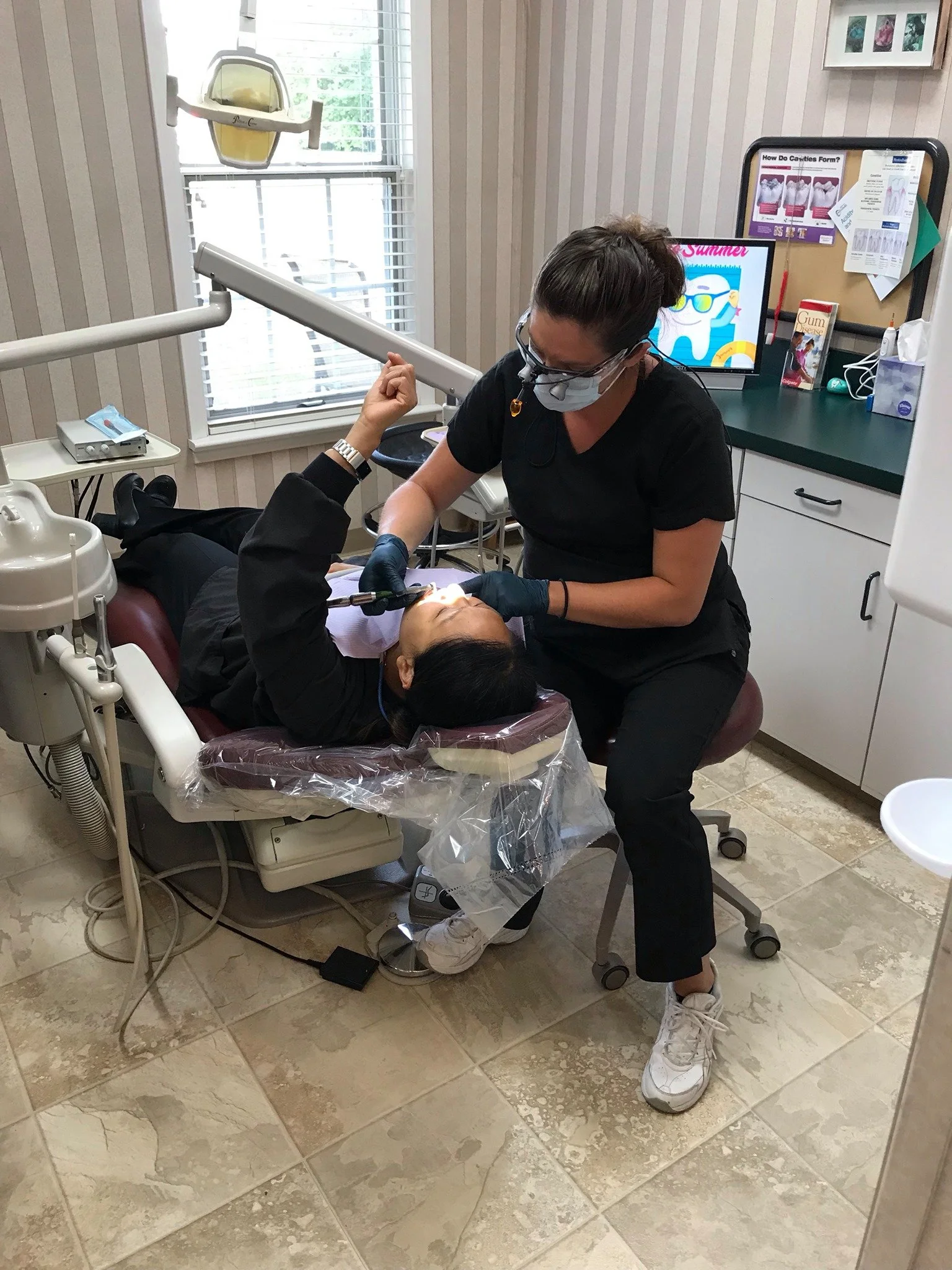 Dental professional attending to a patient lying in a dental chair, with dental equipment and a computer monitor in the background.