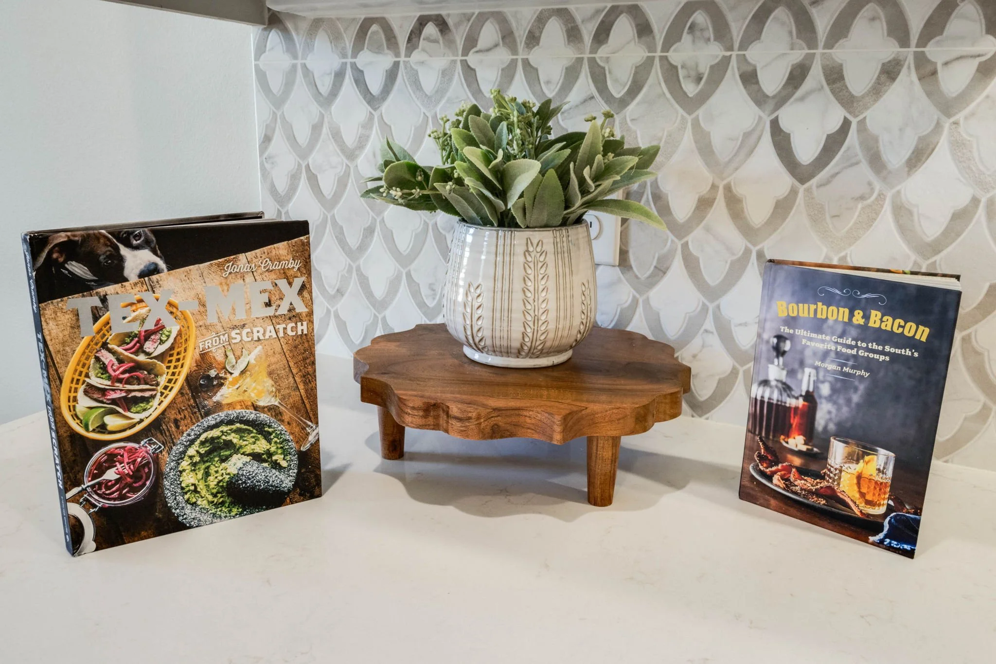 A decorative table with a potted succulent plant and two cookbooks, one on each side of the plant, against a patterned wall.