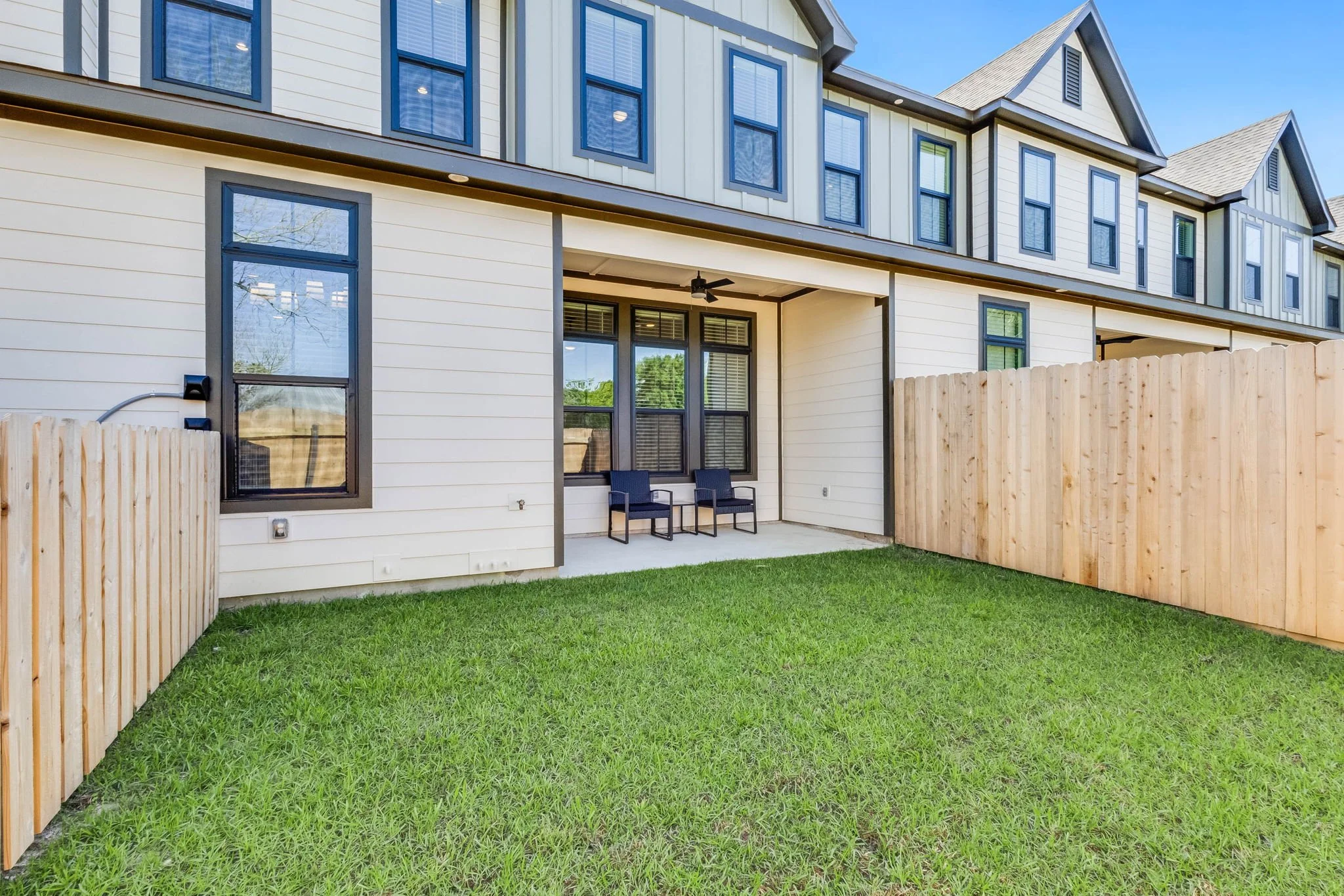 Backyard patio of a townhouse with two chairs, fenced yard, and three-story building with multiple windows.