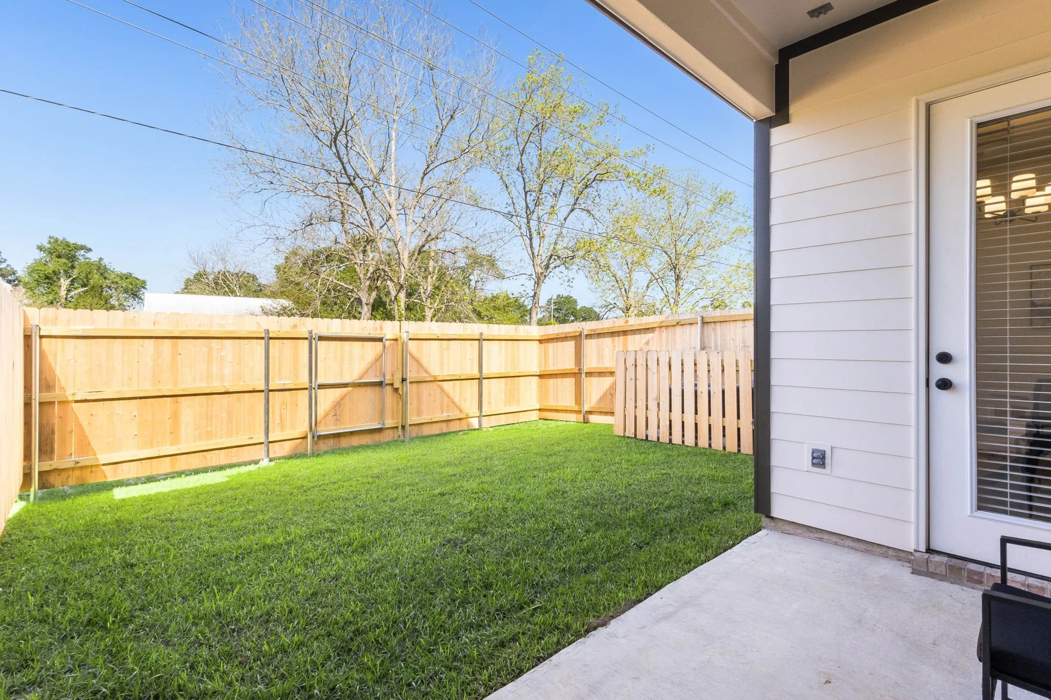 Clean backyard with green grass, wooden fence, and a covered patio area with sliding glass door.