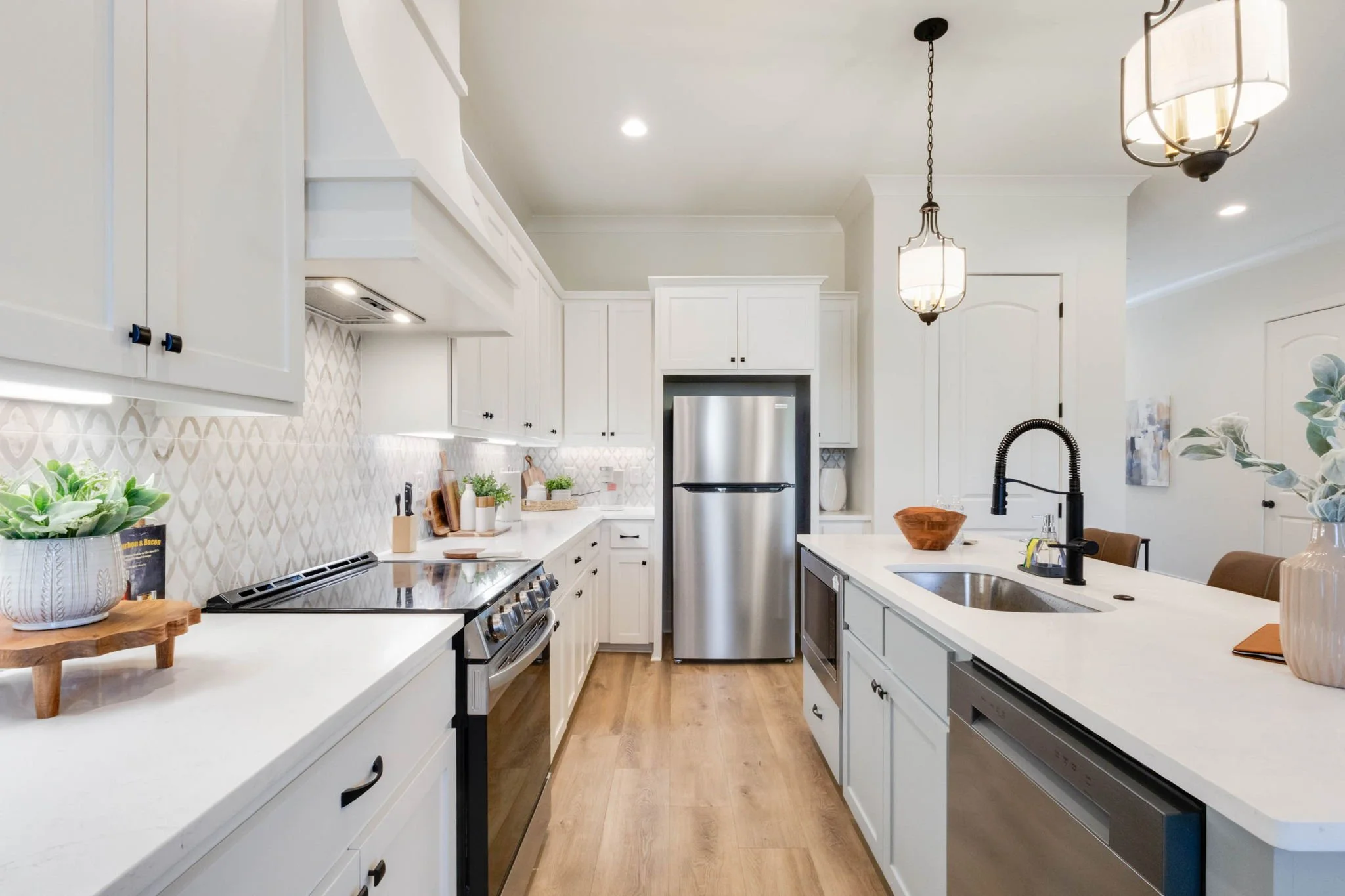 Kitchen with white cabinets, stainless steel appliances, black fixtures, and wooden accents, featuring pendant lights and a central island.