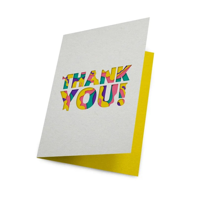 A greeting card with a white front and yellow inside, displaying the colorful message "THANK YOU!" in bold, patterned letters.