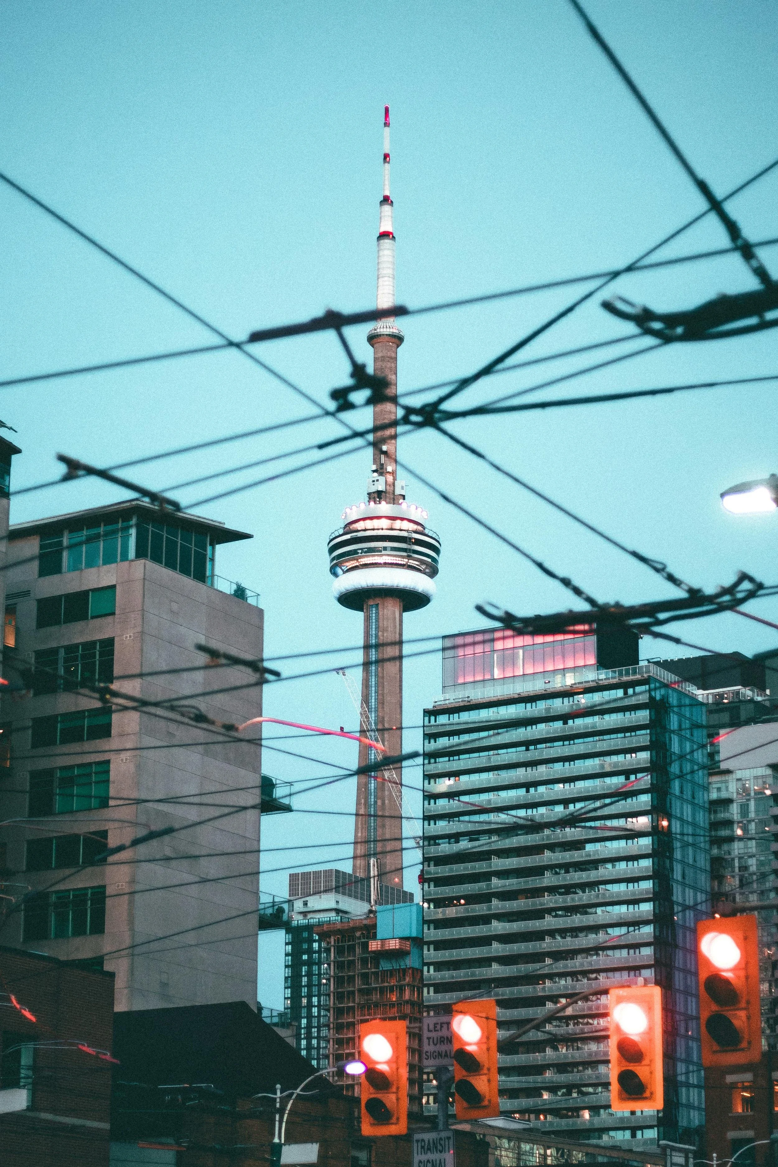 Nighttime view of Toronto skyline featuring the CN Tower amidst surrounding buildings with streetlights and traffic signals in the foreground.