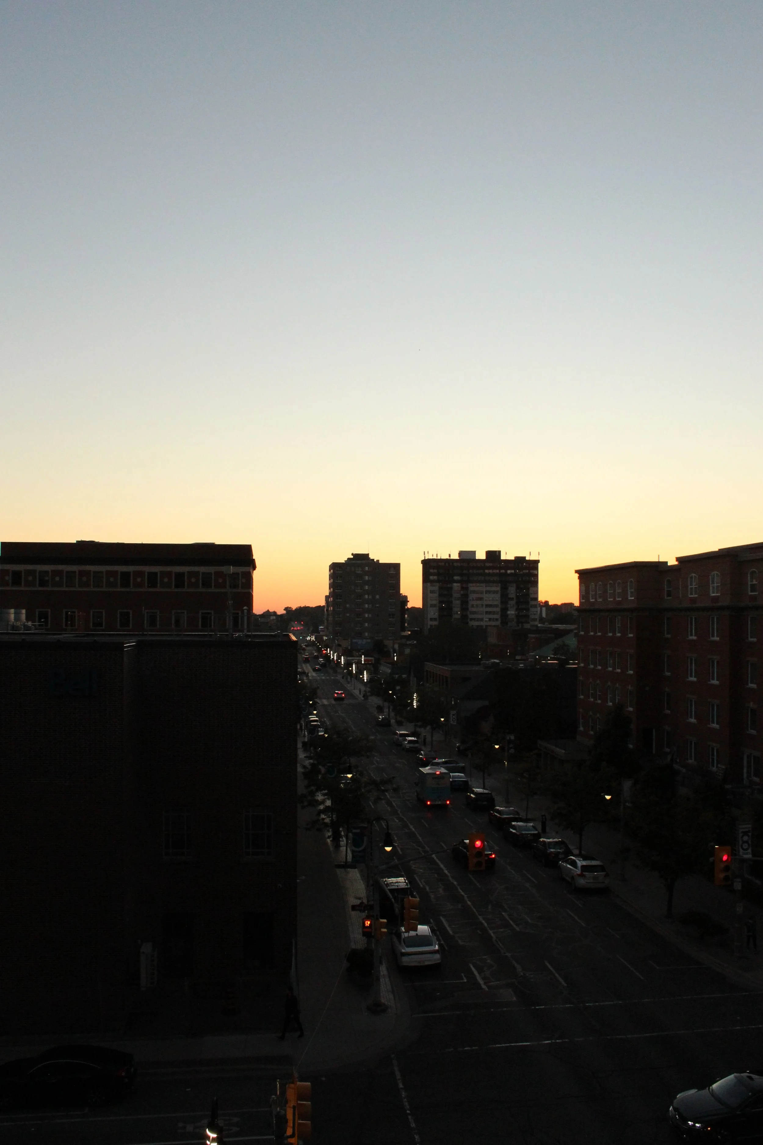 Urban city street at sunset with buildings, cars, and traffic lights