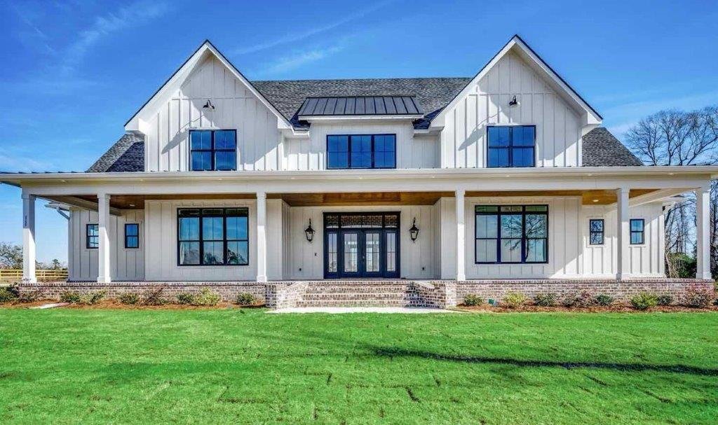 Modern farmhouse-style two-story home with white vertical siding, black-framed windows, a front porch, and a manicured lawn.