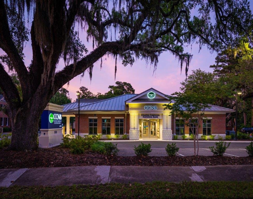 A bank building with neon signs, trees, and a purple sunset sky.