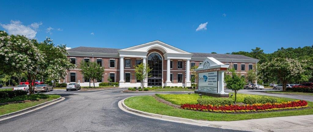 A large brick hospital building with a white entrance and a sign in front reading