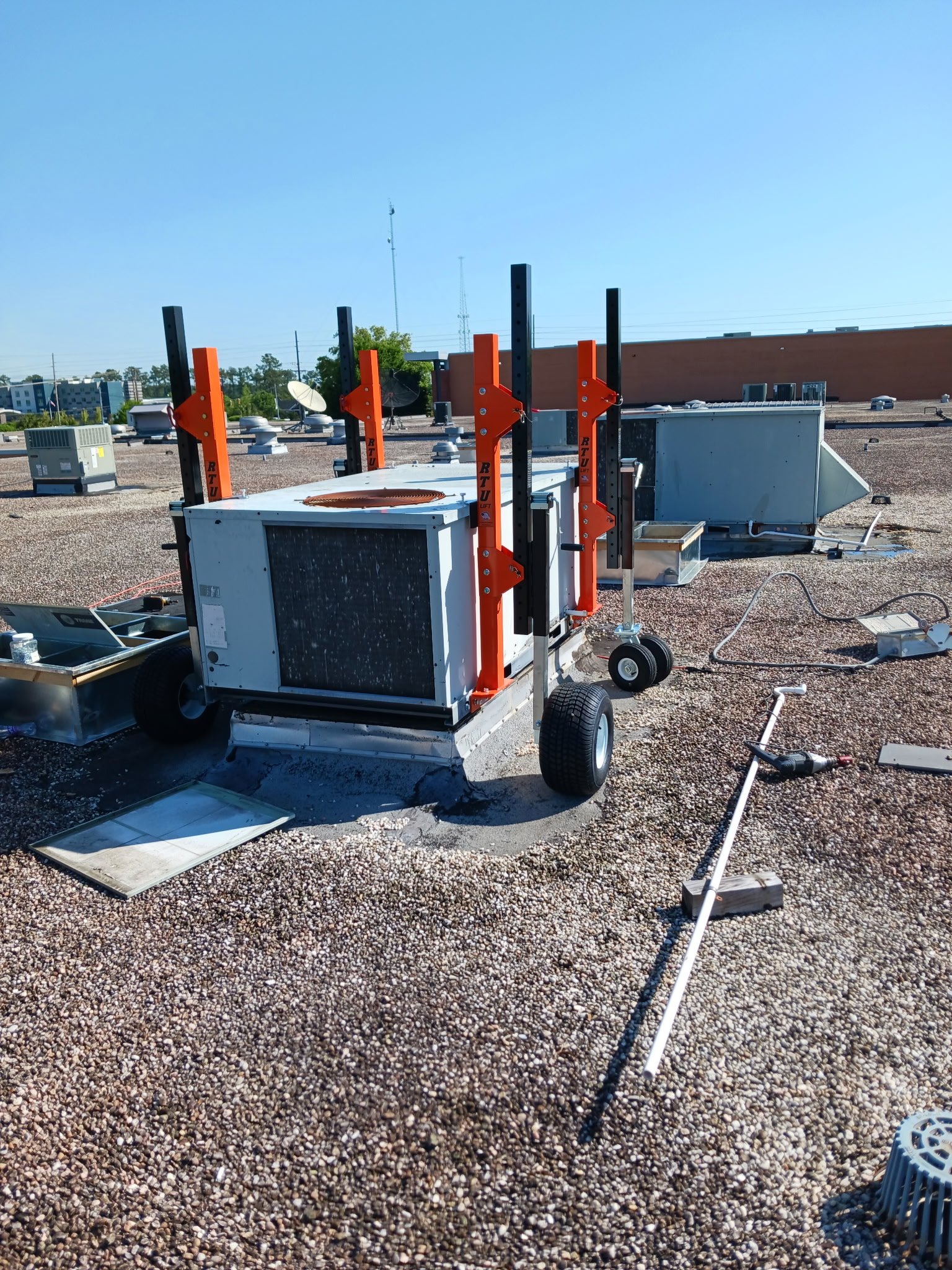 Rooftop HVAC units and mechanical equipment with orange pipe supporting structures and tools scattered on gravel surface.