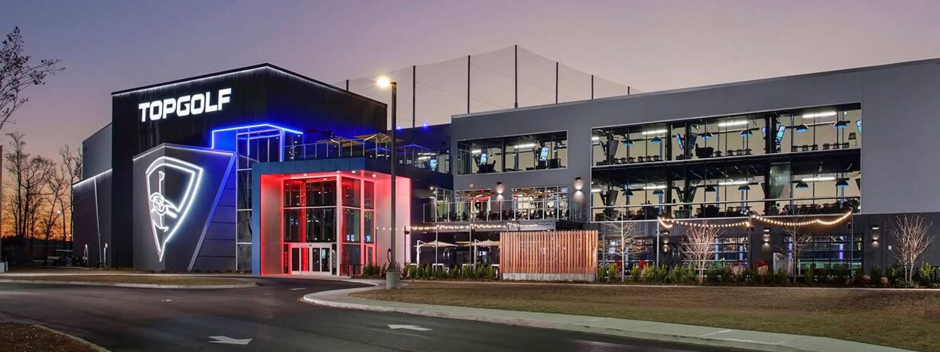 Outdoor view of a modern fitness center with illuminated signage and large windows showing workout equipment inside, during dusk or early evening.