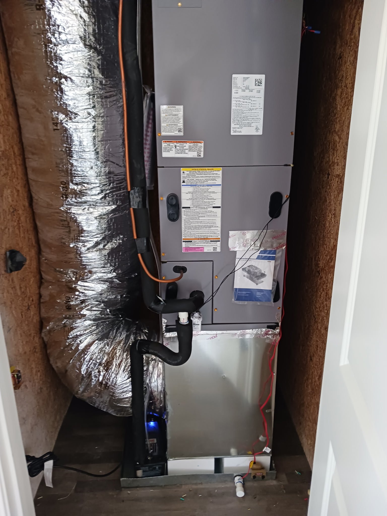 An HVAC air handler unit installed in a small closet with insulated ductwork, electrical wiring, and a metal panel.