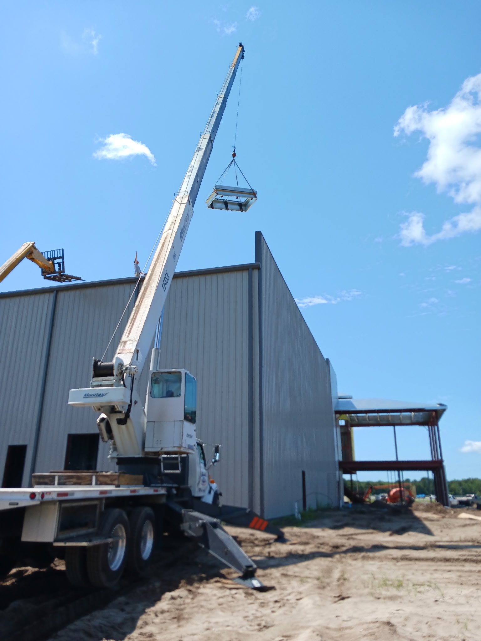 A crane lifting a large metal platform at a construction site next to a gray industrial building.