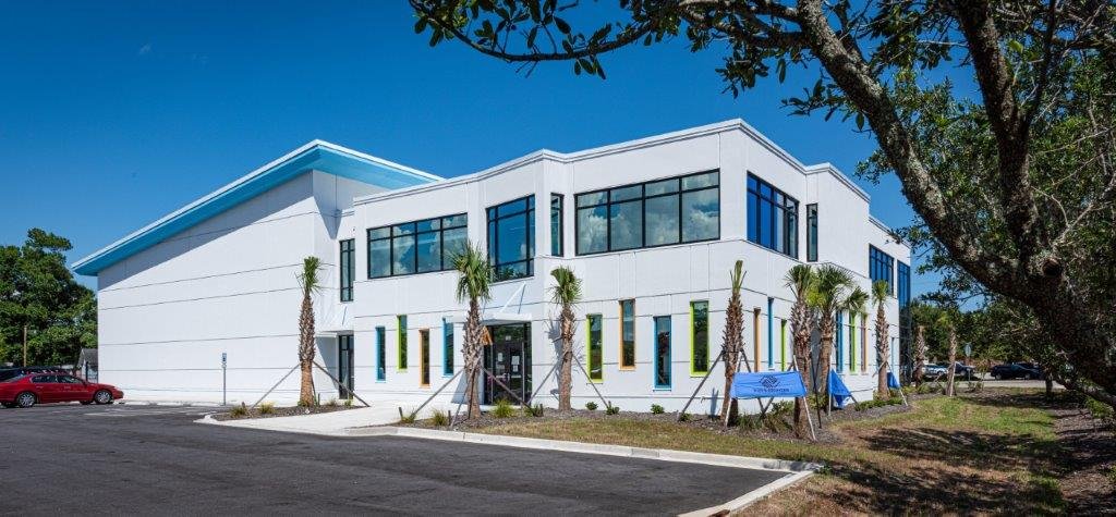Modern white building with large windows and palm trees outside under a blue sky