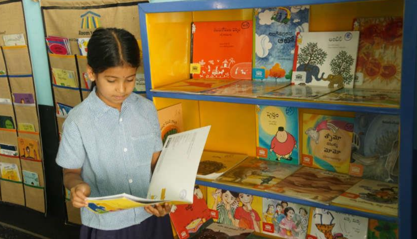 Ein indisches Mädchen hält ein Buch in den Händen. Sie steht vor einer Bibliothek