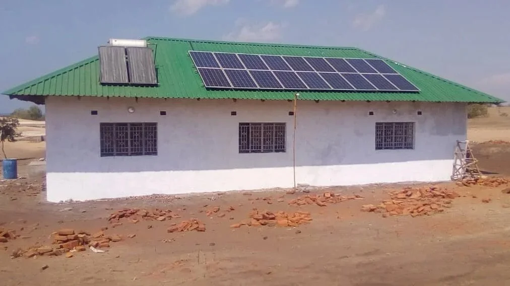 Einfaches weißes Haus mit grünem Dach, auf dem eine Fotovoltaik-Anlage angebracht ist.