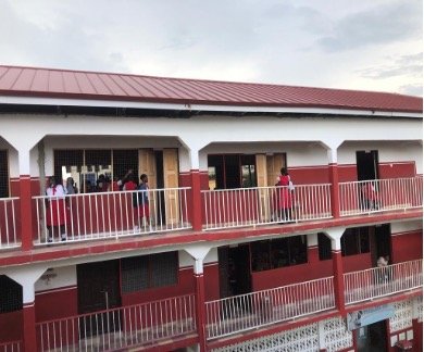 Rot-weißes Gebäude mit zwei sichtbaren Etagen. Auf der oberen sind Personen, darunter Schulkinder, erkennbar.