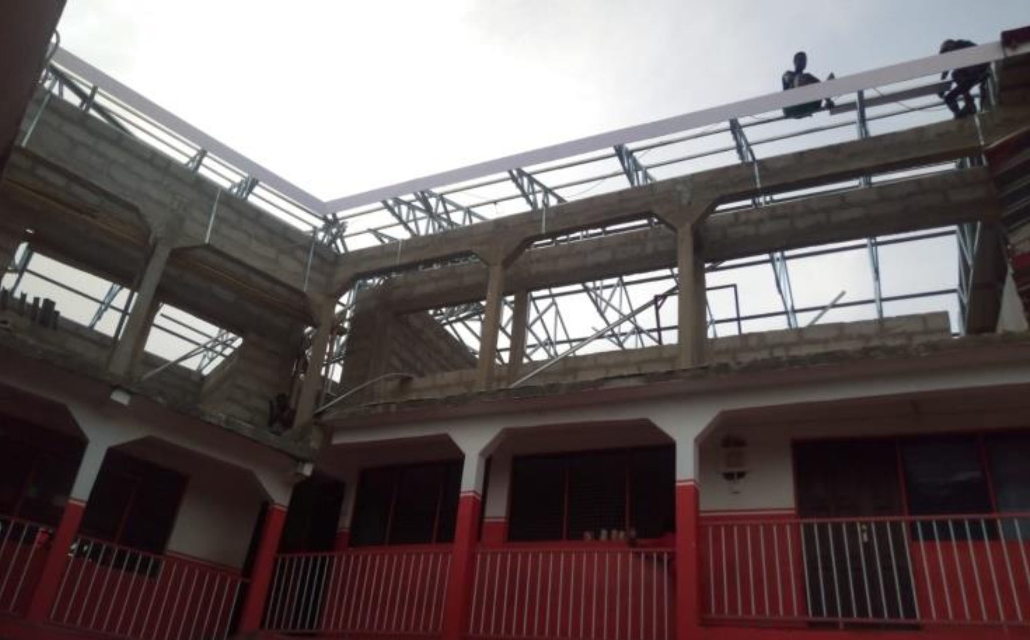 Aufsicht auf den Bau von zusätzlichen Etagen auf einem weiß-roten Gebäude. Oben sind Gerüste und Bauarbeiter zu sehen.