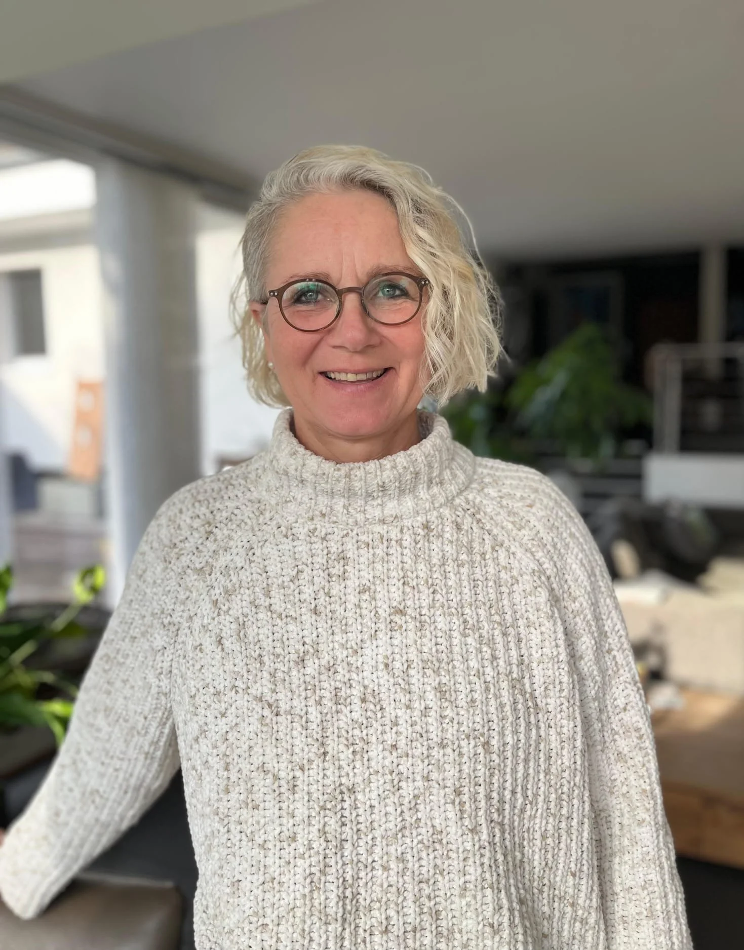 Frau mit grauer welliger Kurzhaarfrisur und Brille, die in die Kamera lächelt.