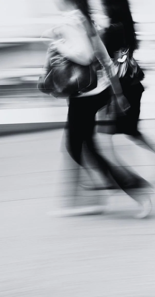 A blurred black and white photo of a person walking, carrying a bag, in an urban setting.