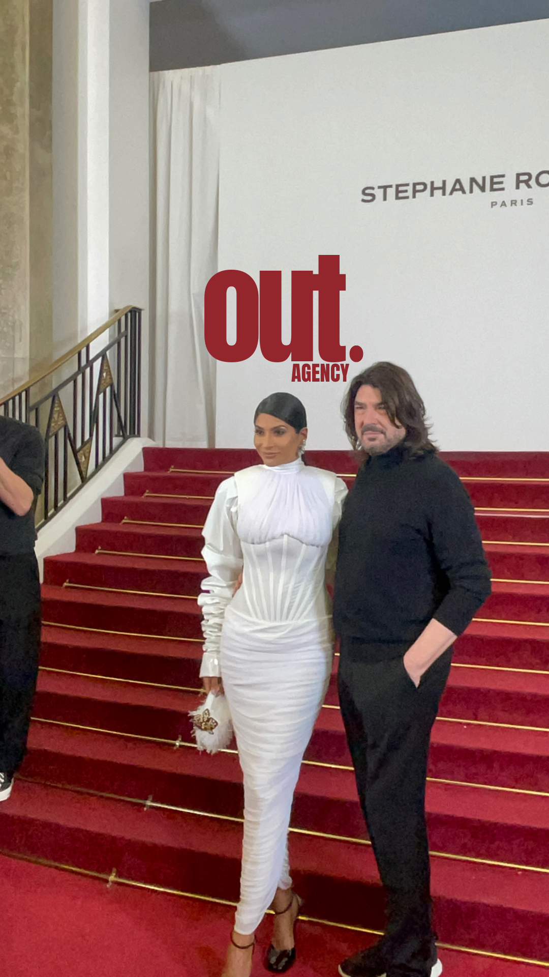 Deux personnes posent sur un escalier rouge avec une bannière qui dit 'out. AGENCY' et un mur avec des inscriptions 'STEPHANE ROGER PARIS'.