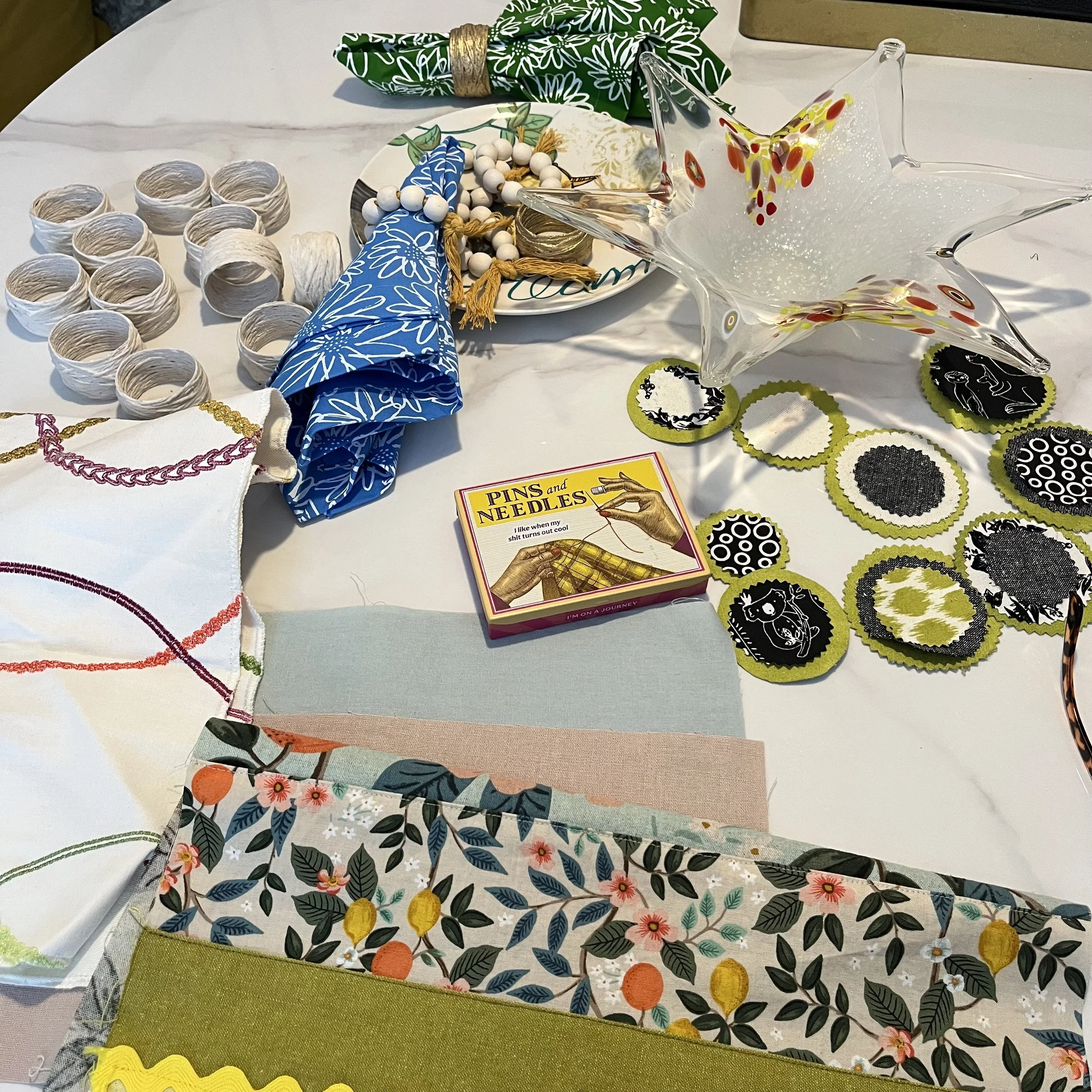 A table decorated with colorful napkins, a star-shaped glass dish, patterned paper templates and various decorative objects including a small plate with bead jewelry, and circular fabric cutouts with black and white designs.