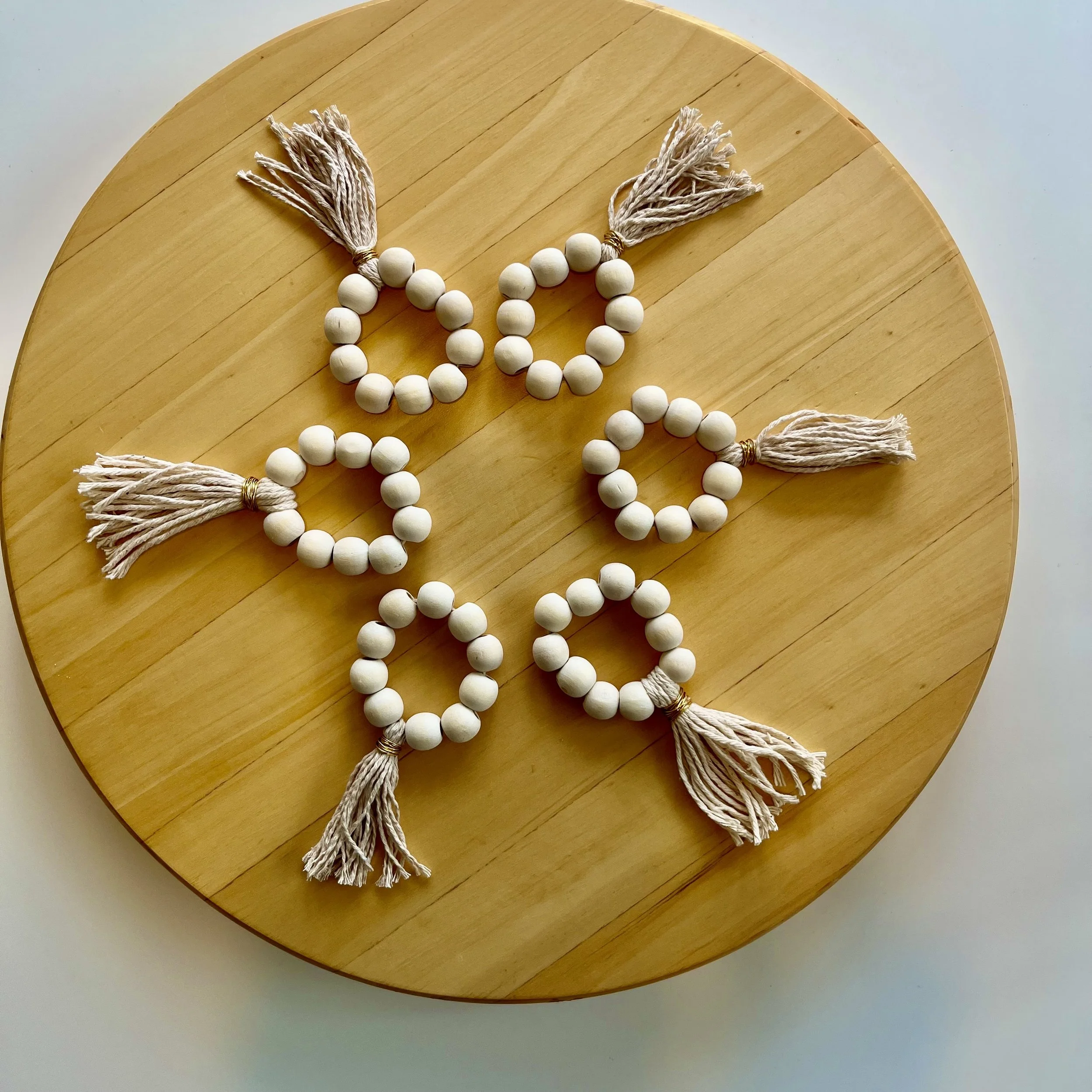 Six beaded napkin rings with handmade wool tassels arranged in a flower pattern on a round wooden surface.