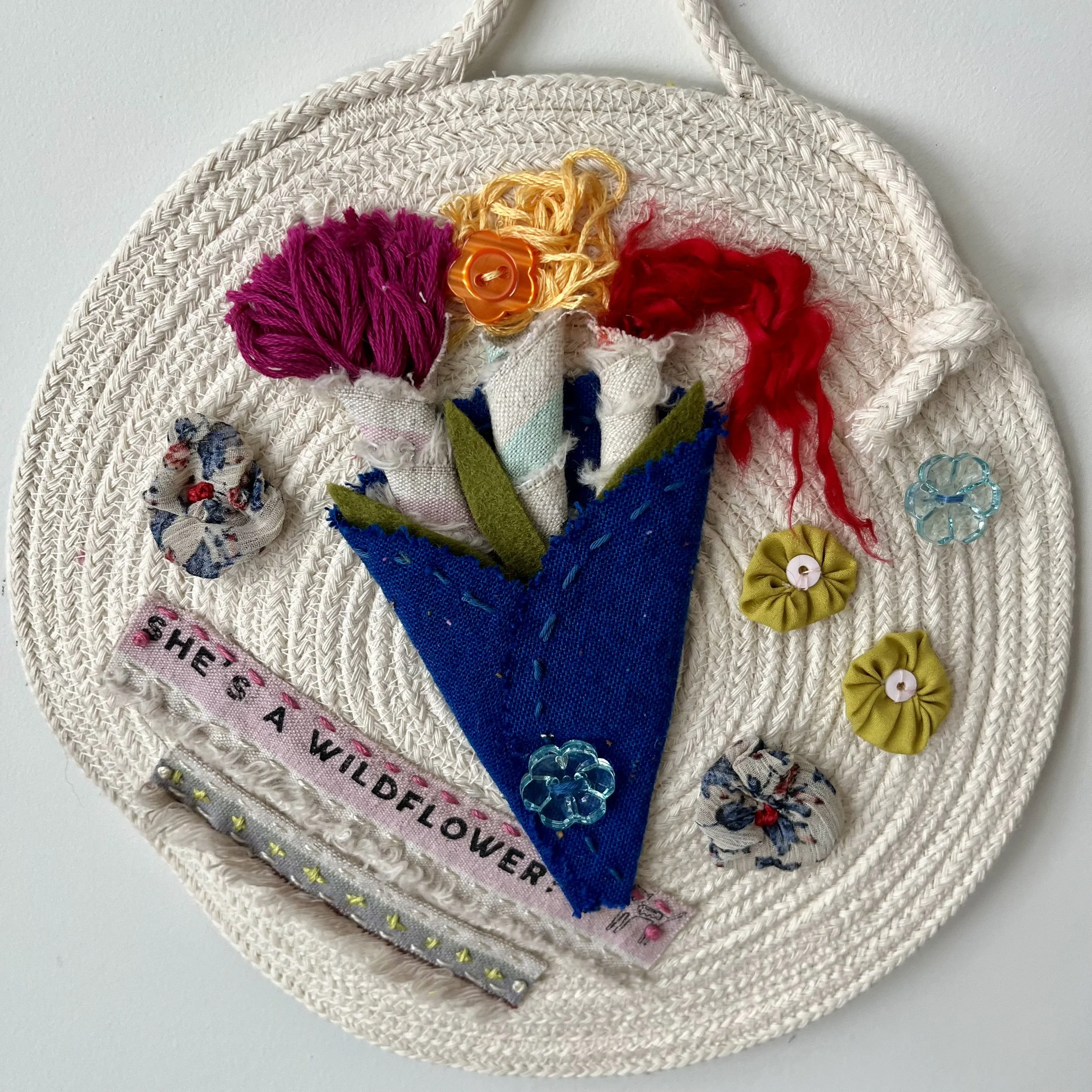 A small circular cotton rope hanging with hand sewed linen and silk flowers, wool thread and hand dyed sheep's wool.