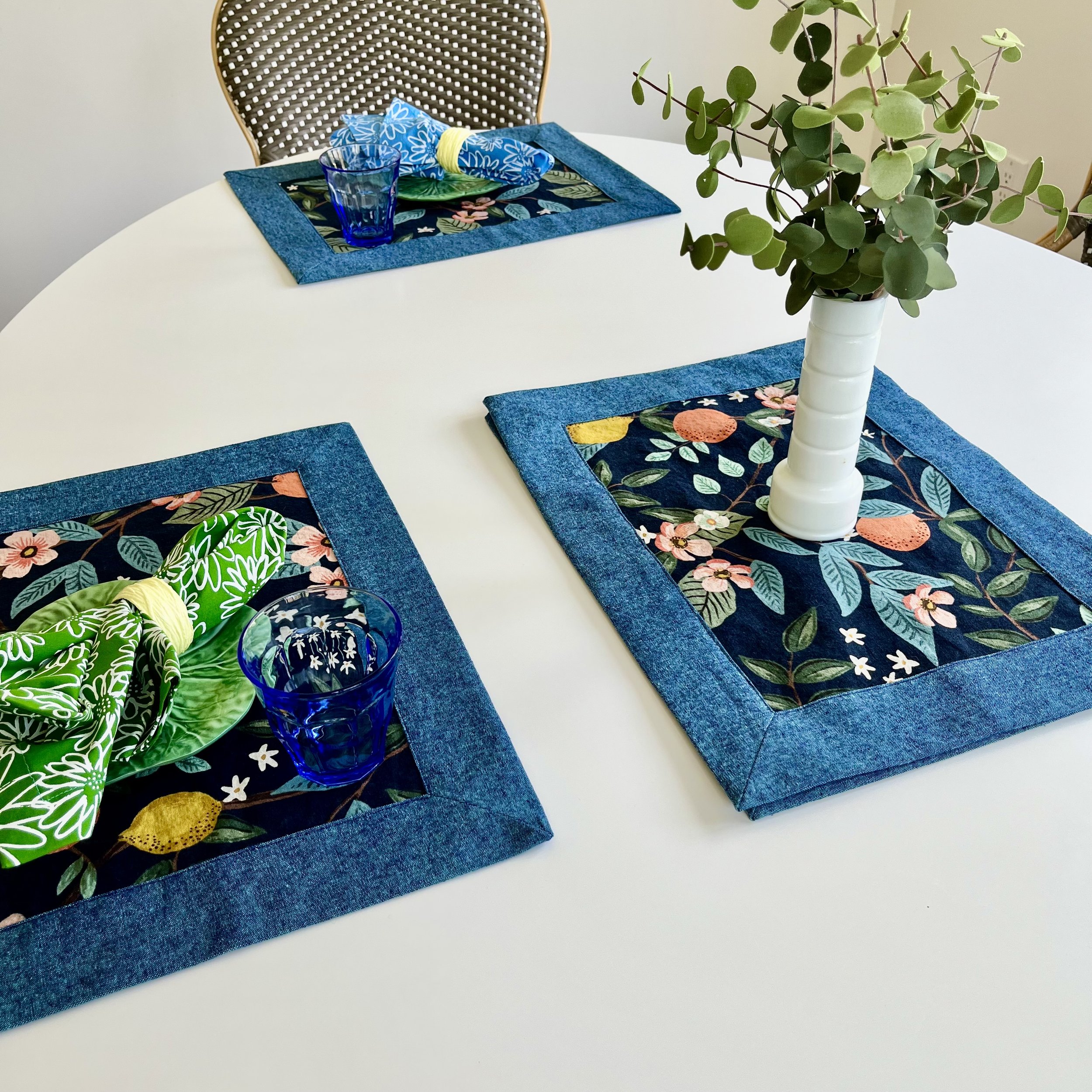 Set of colorful cotton linen fabric placemats featuring a floral and fruit design with a blue border. 