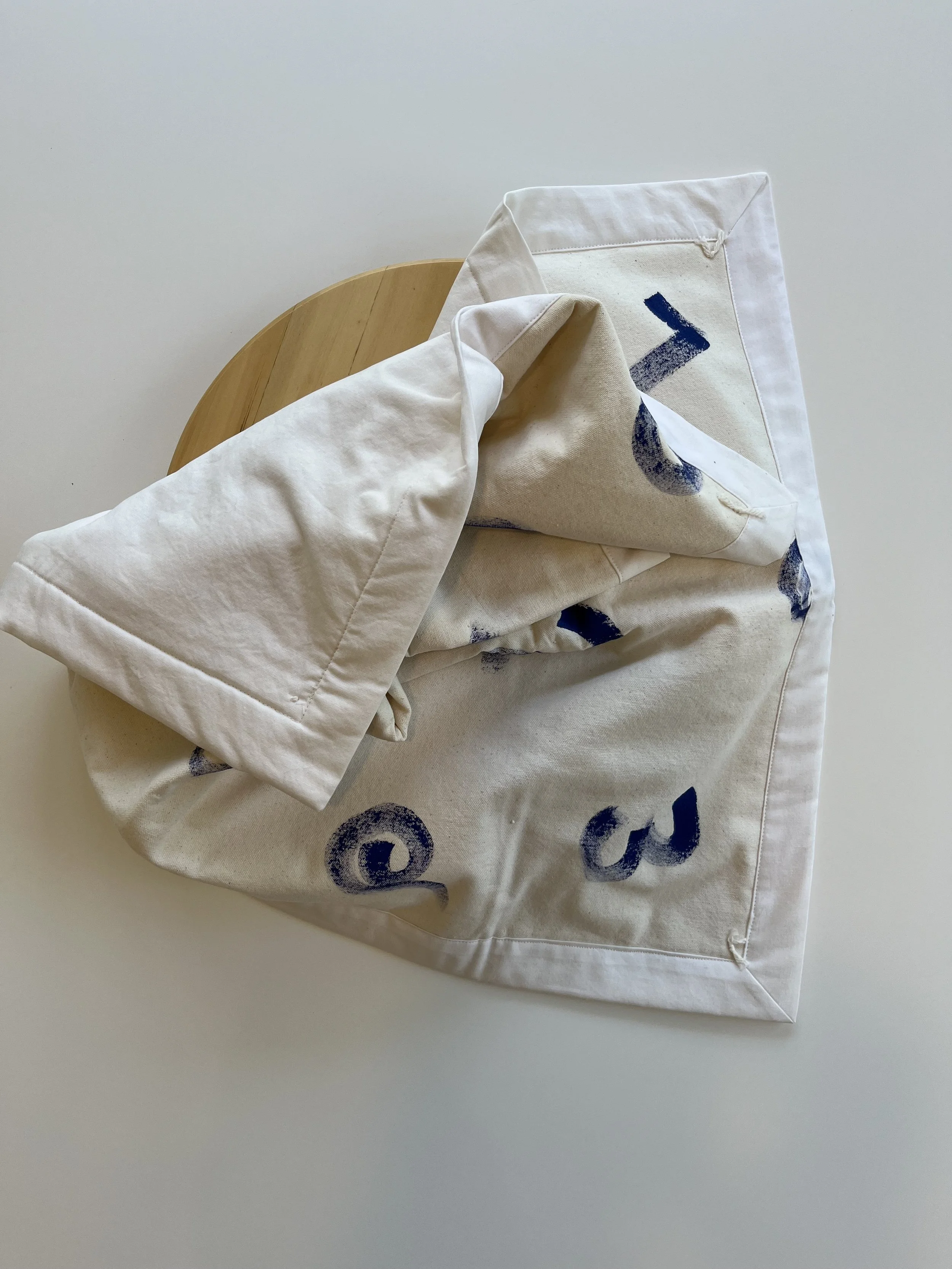 A cotton linen baby floor blanket with blue hand block printed abstract shapes. 