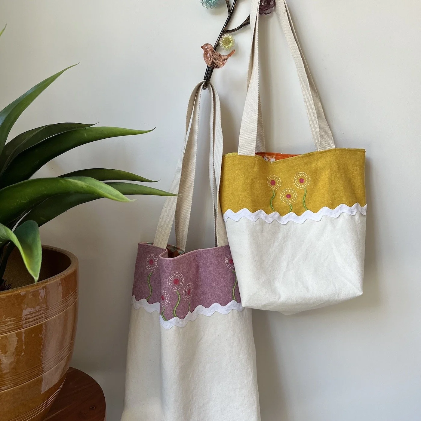 Two market cotton canvas tote bags, hand printed flowers and embroidery, one yellow and white and one pink and white.