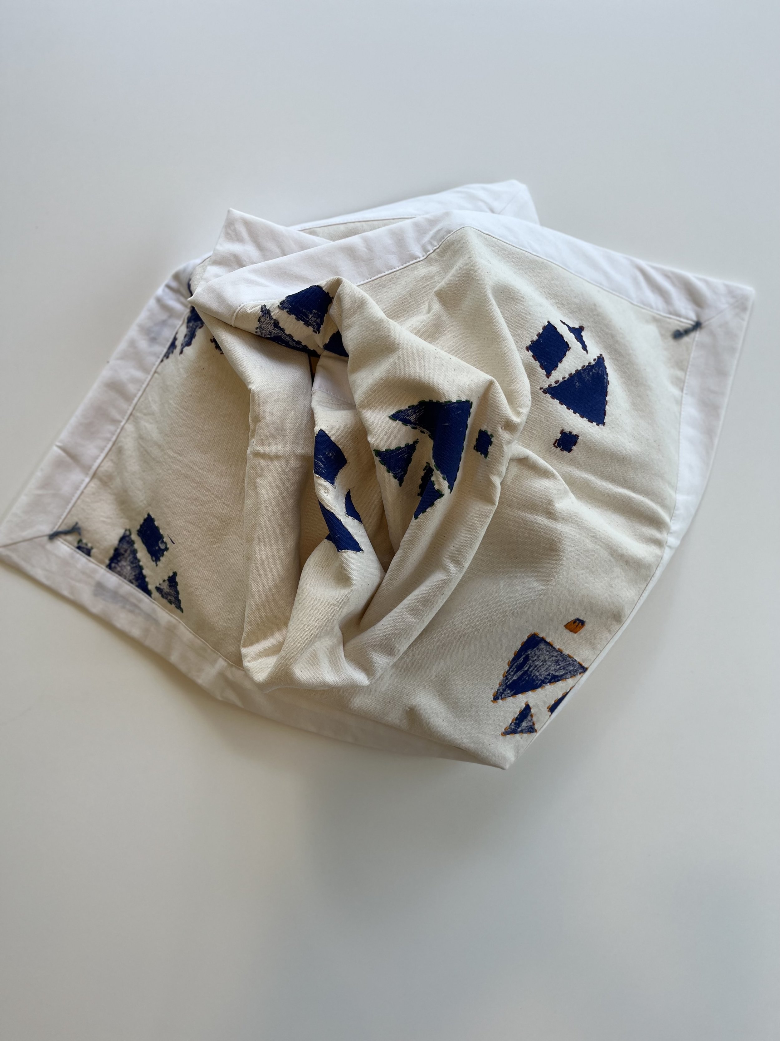 A hand printed canvas baby floor blanket with hand printed blue geometric patterns on a white background.