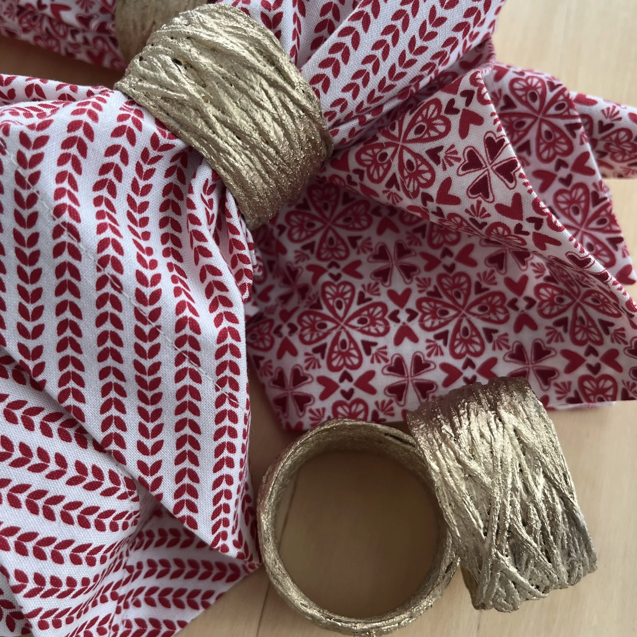 Cotton napkins with red and white heart and leaf pattern, held with handmade gold napkin rings.