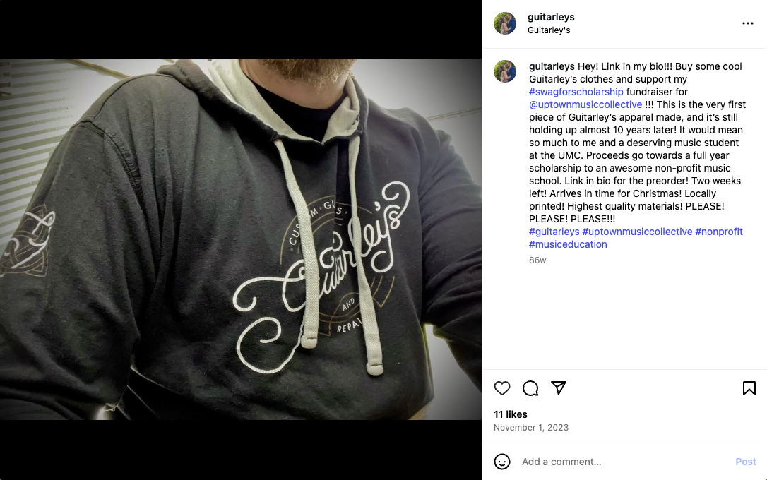 Close-up of a person wearing a black hoodie with a Guitarley's logo on the front and sleeve, with drawstrings hanging down.