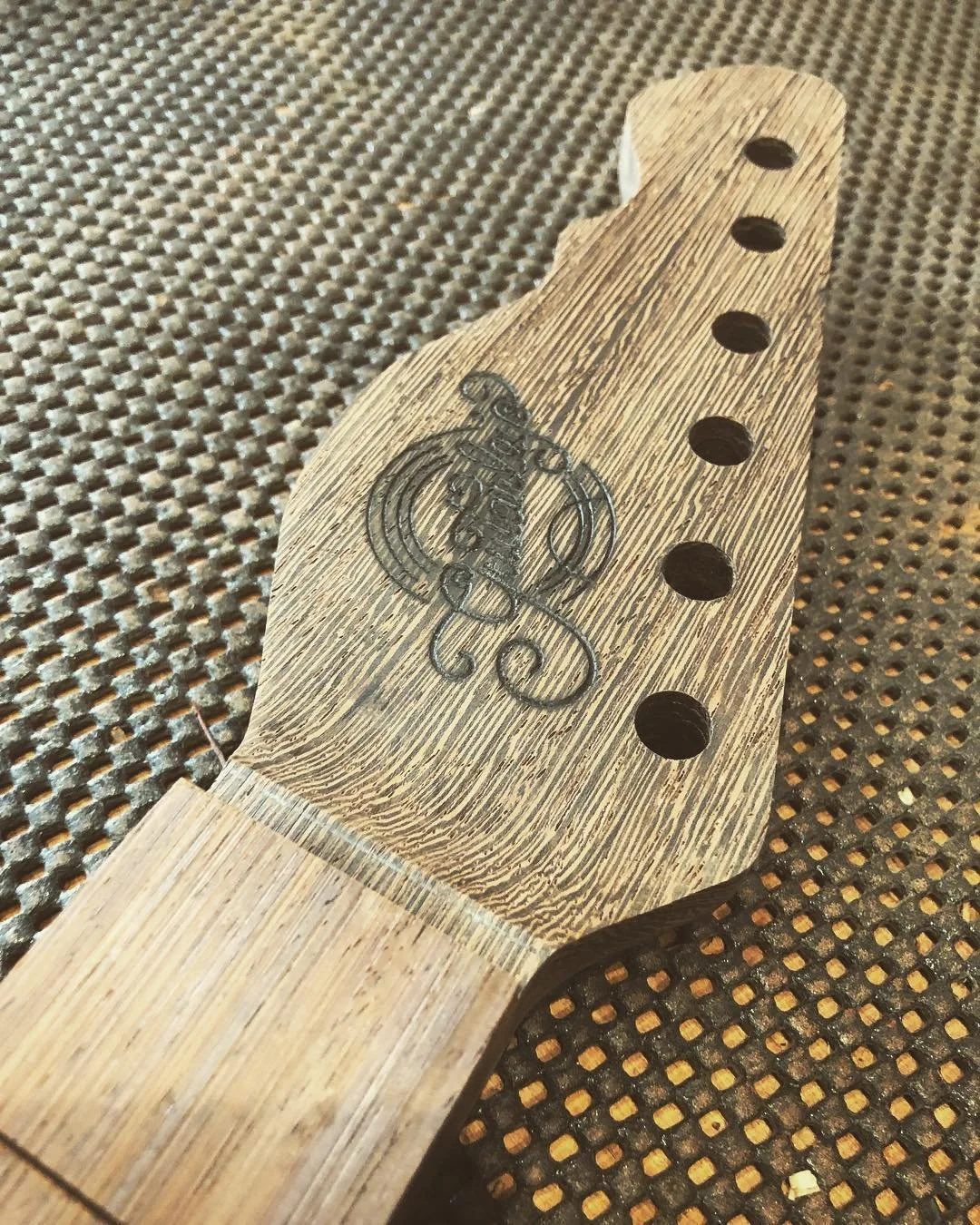 Close-up of a guitar headstock with a logo and five tuning peg holes.
