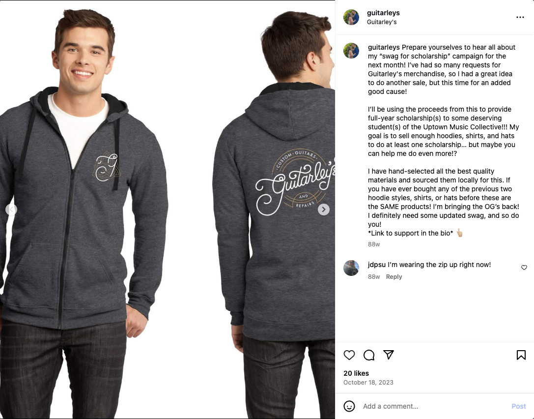 A young man modeling a dark gray zip-up hoodie with a small white logo on the front and a large logo on the back, both featuring the brand name Guitarley's. The man is shown smiling facing forward and wearing the hoodie with dark plaid pants against