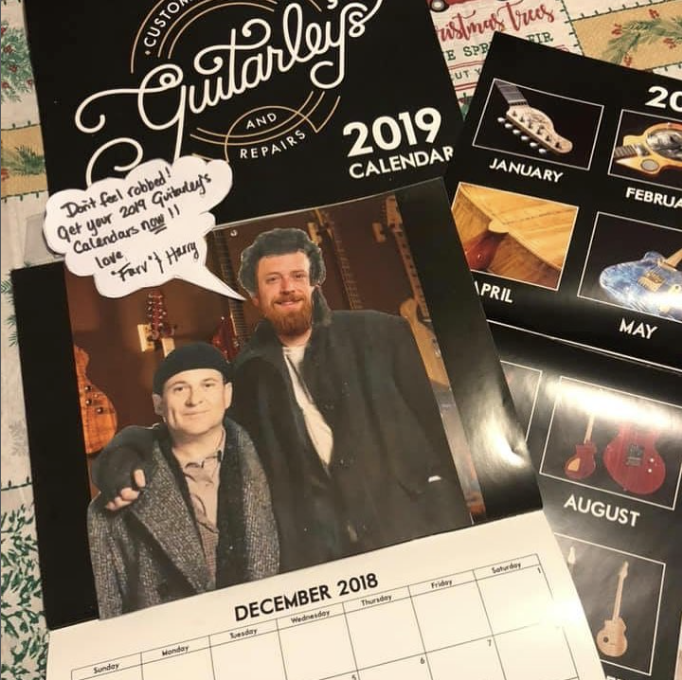 2019 calendar for Guitar's and Repairs with a photo of two men, one with curly hair and a beard, and a speech bubble that reads, "Don't feel robbed! Get your 2019 Guitar's Calendars!!! Love, Fary & Hany." The calendar features images of guitars for e
