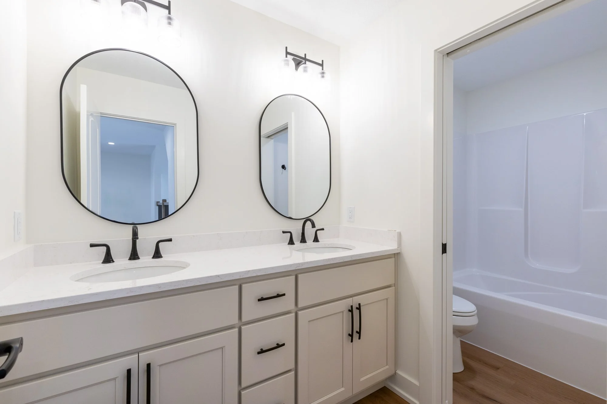 Beautiful photograph of secondary full bathroom featuring double vanity, plenty of lighting, and seperate toilet and bath.