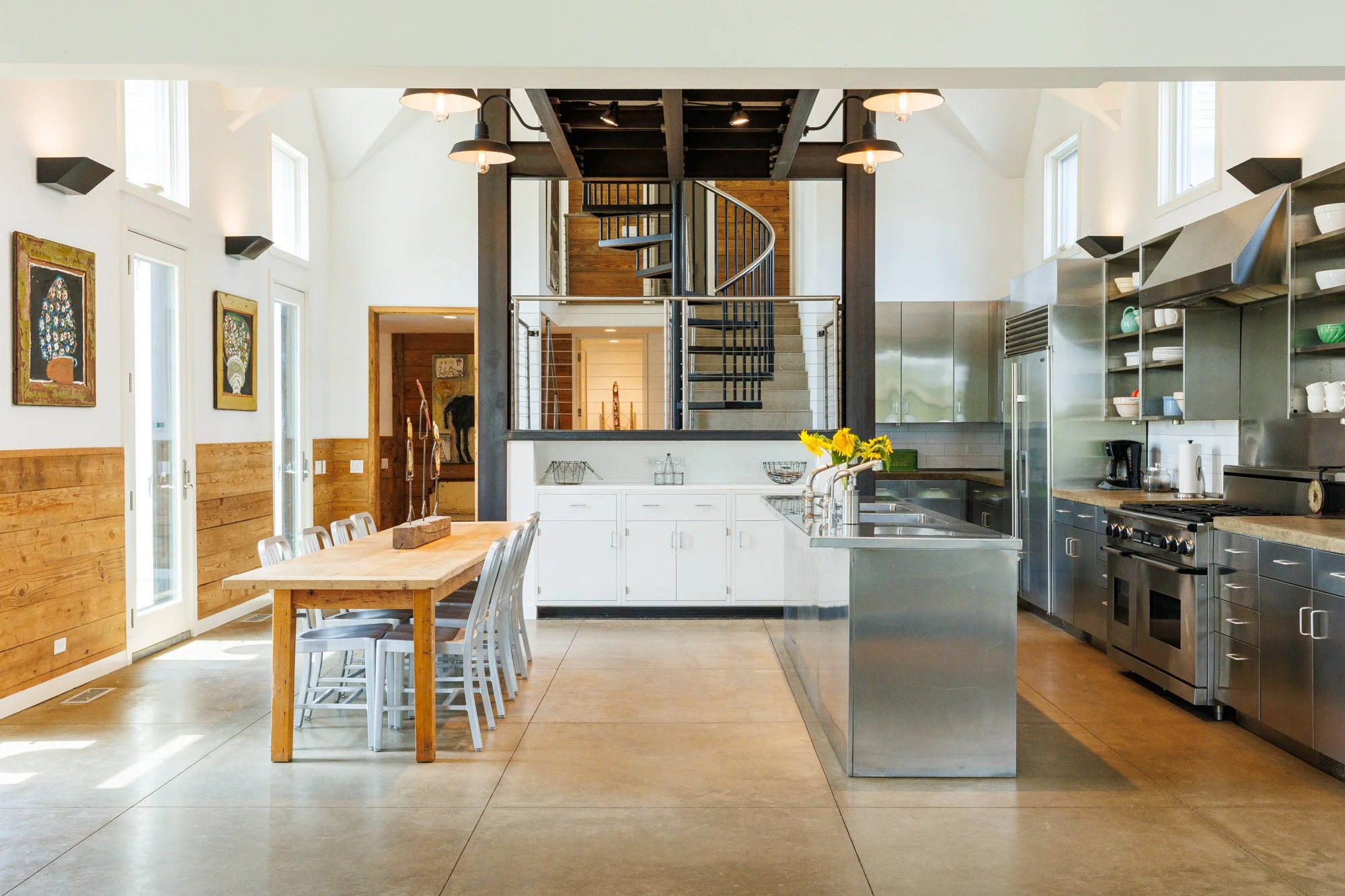Stunning architectural photo of a custom kitchen. Stainless steel throughout, tons of windows with natural lighting, concrete polished floors, and a staircase leading to a an amazing suspended catwalk