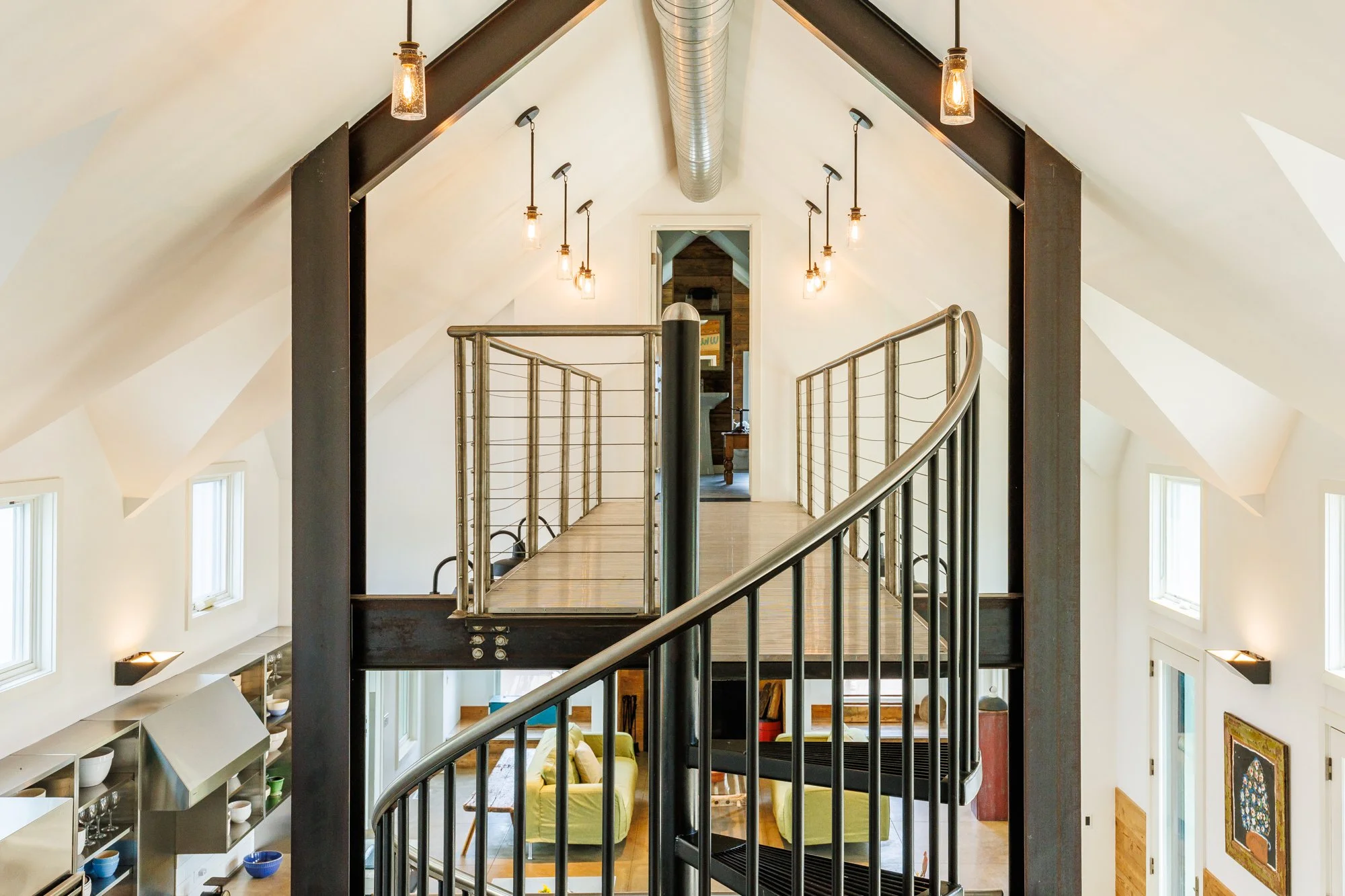 Architectural photo of a catwalk above the kitchen area leading to a private guest room. featuring a beautiful spiral staircase leading to the catwalk, and suspended lighting throughout.