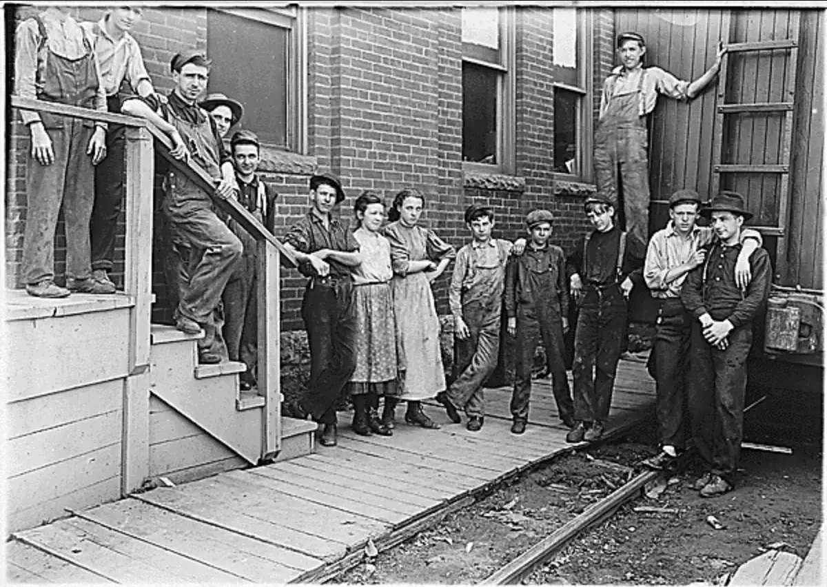 Black-and-white photo of mill workers, including children, outside factory building.