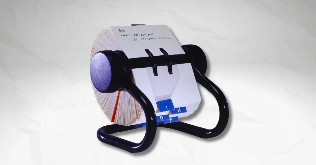 A 1950s executive desk with a full Rolodex prominently displayed, hundreds of business cards on the rotating spindle, representing the moment professional value became countable.