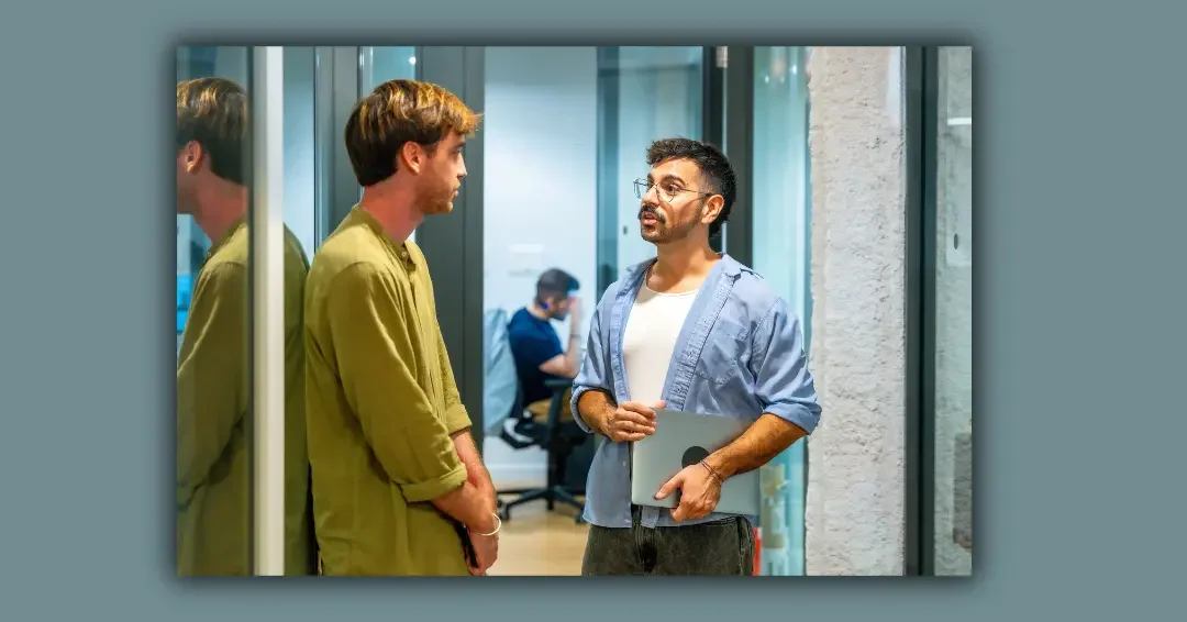 Two men are standing in a modern office hallway, engaged in a serious conversation.