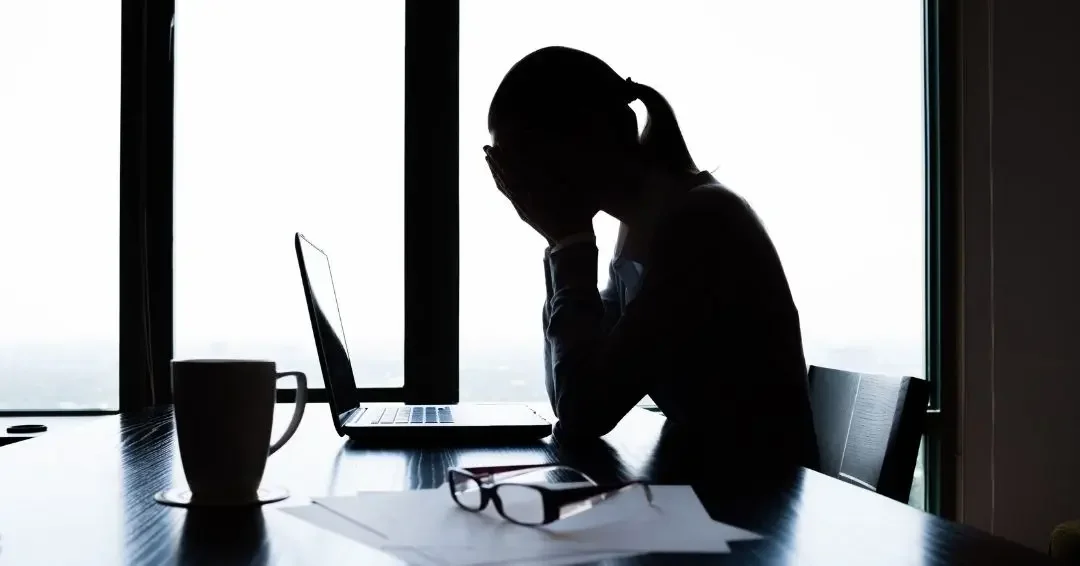 manager sitting at her desk, head in hands indicating overwhelm