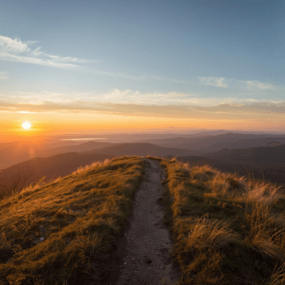 An inspirational photo of a trail ending at the top of a vast vista at the top of a hill at sunrise
