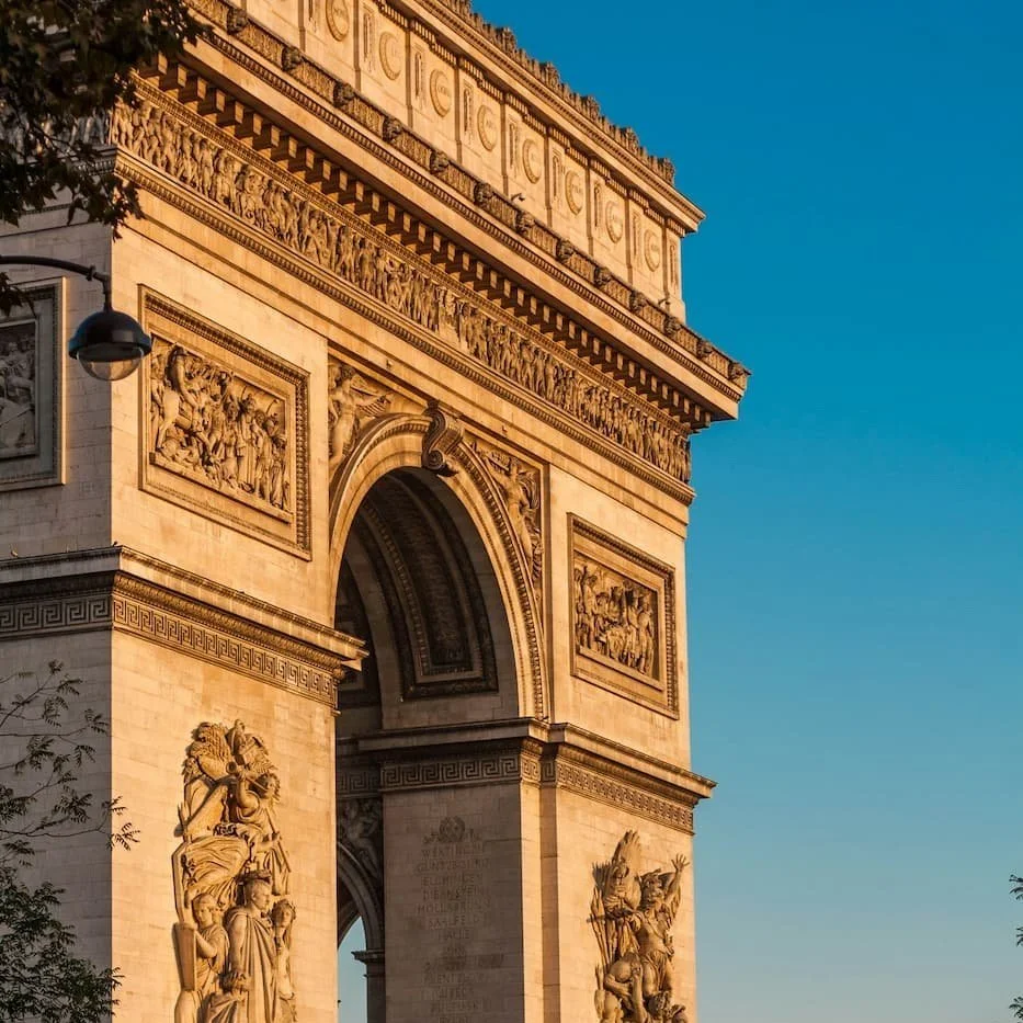 Close-up of the Arc de Triomphe in Paris, France, showing detailed stone sculptures and ornate carvings against a clear blue sky.