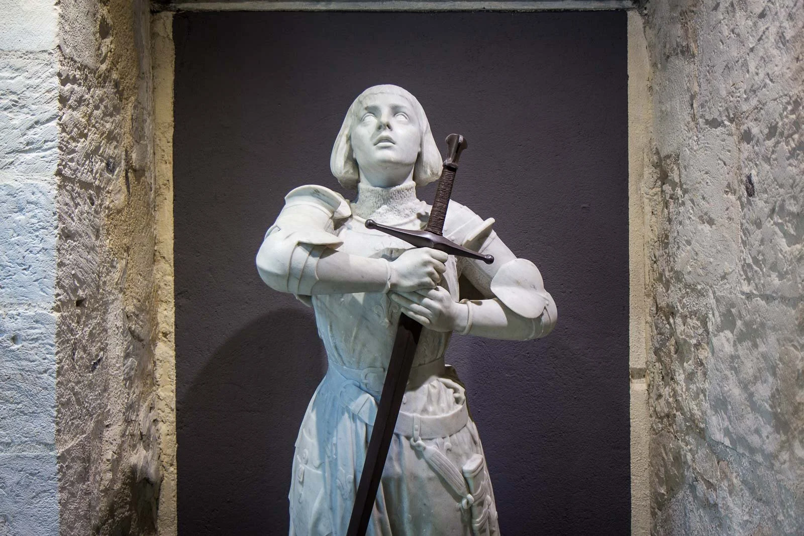 Private day-trip for French Voyage clients to visit the resting place of Joan of Arc, featuring a statue of her as a young woman in medieval armor holding a sword and looking upward.