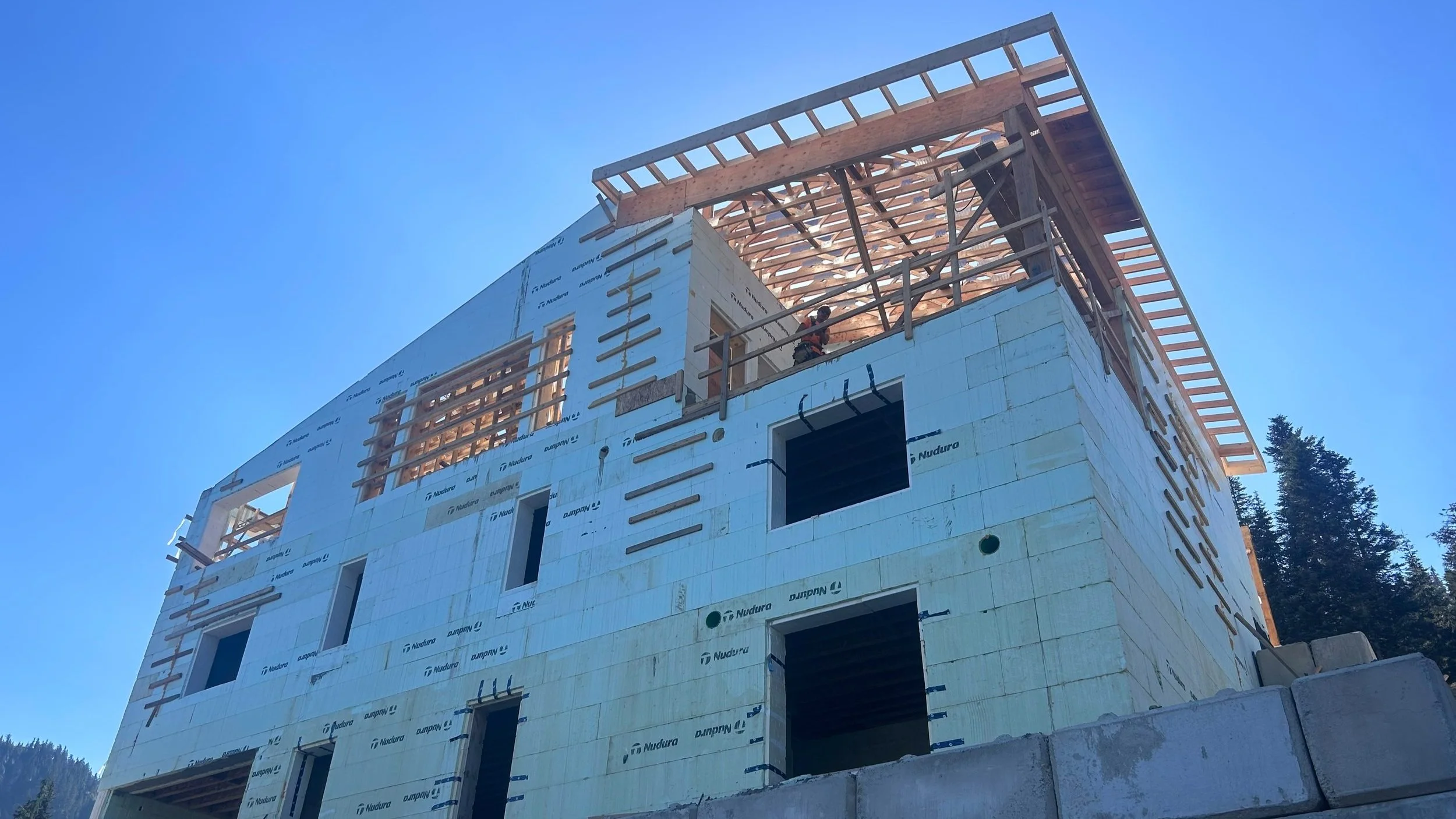 Multi-story building under construction with ICF framing, blue sky background and surrounding trees.